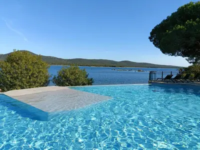 a swimming pool with chairs and a view of a lake at Appt neuf 2-4 pers avec loggia - Piscine chauffée - Bord de mer - Corse du Sud- Bonifacio in Pianottoli-Caldarello