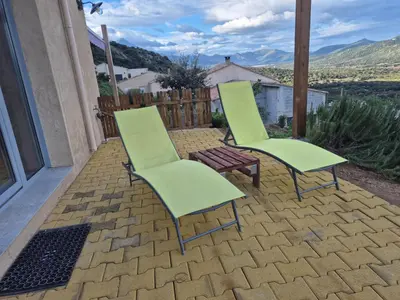 two green chairs and a bench on a patio at Vos vacances à 3 minutes de la mer in Belgodère
