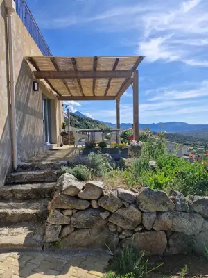 a wooden pergola on a house with a stone wall at Vos vacances à 3 minutes de la mer in Belgodère