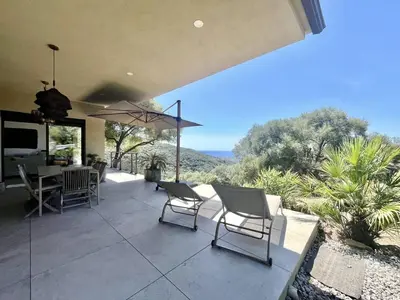 a patio with chairs and a table and an umbrella at Villa d'architecte avec vue mer imprenable et piscine chauffée in Viggianello