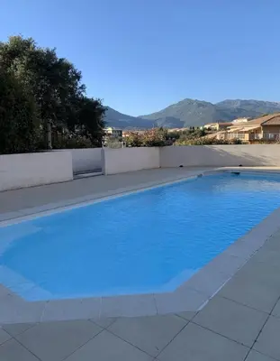a large blue swimming pool with mountains in the background at Appart résidence avec piscine in Propriano