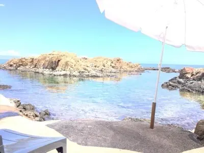 an umbrella sitting on a beach next to the water at Magique Creek, piscine naturelle dans les rochers in Zonza