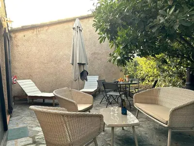 a patio with chairs and an umbrella and tables at Mini-villa à 1 minute de la plage de Santa Giulia in Porto-Vecchio