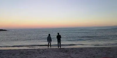 two people standing on the beach looking at the ocean at Auberge de Cannedda in Sari Solenzara