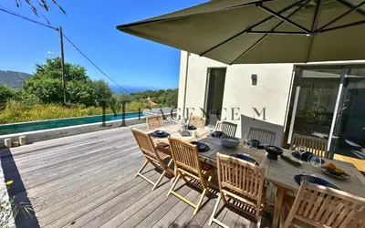 a wooden table with chairs and an umbrella on a deck at Villa Giuliana Paisible & spacieuse AREGNO in Aregno