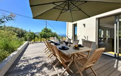 a wooden table with chairs and an umbrella on a deck at Villa Giuliana Paisible & spacieuse AREGNO in Aregno