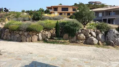 a stone retaining wall in front of a house at Maison au calme avec vue magnifique in Sari Solenzara