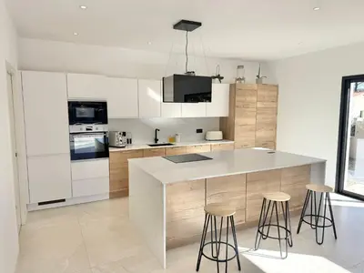 a kitchen with white cabinets and a counter and stools at Villa Porto-Vecchio avec piscine in Lecci