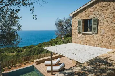 a stone house with a table and a swimming pool at Casi di Mare in Cargèse