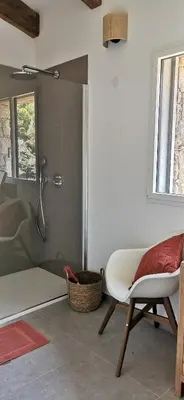 a bathroom with a shower and a chair and a tub at Casa PETRA, typique en pierres au coeur du maquis, 2 pers, Piscine in Pietrosella