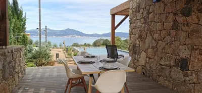 a wooden table with chairs and a laptop on a patio at Casa PETRA, typique en pierres au coeur du maquis, 2 pers, Piscine in Pietrosella