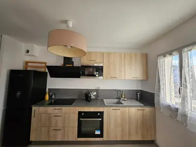 a kitchen with wooden cabinets and a black refrigerator at Appartement moderne à Lucciana avec terrasse ensoleillée. in Lucciana