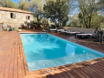 a pool with a wooden deck and a patio with tables at Les Bergeries de Petralonga in Sotta
