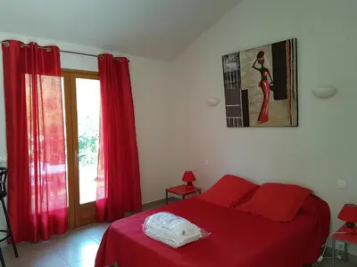 a bedroom with a red bed with red curtains and a window at Studio pour 2 personnes à 700m de la plage de palombaggia in Porto-Vecchio
