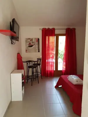 a bedroom with red curtains and a table with chairs at Studio pour 2 personnes à 700m de la plage de palombaggia in Porto-Vecchio