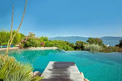 a swimming pool with a wooden walkway next to the water at Charmante maison à Olmeto avec piscine partagée in Olmeto