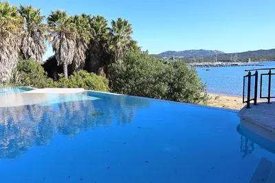 a large swimming pool next to a body of water at Casa di Daisy - T2 les pieds dans l'eau et piscine in Pianottoli-Caldarello