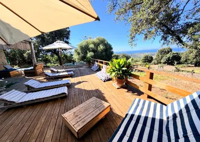 a wooden deck with lounge chairs and an umbrella at Maison de maître en pierre de 1831 avec vue sur la mer à Porticcio in Porticcio