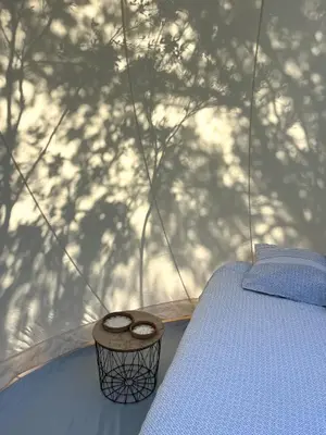 a bed in a tent with a wooden holder and shadows at Bulle du Fangu in Galeria