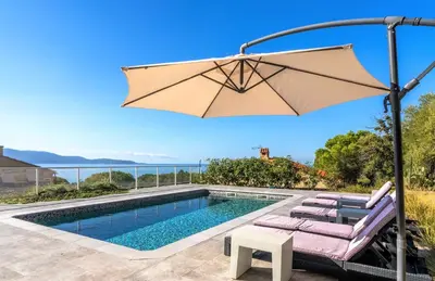 a swimming pool with an umbrella and lounge chairs next to a pool at Villa le Palmier 10 personnes piscine, vue mer, plage in Olmeto