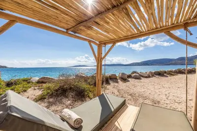 a view of the beach from a porch with a swing at Villa Cala Rossa pieds dans l'eau Porto-Vecchio in Lecci