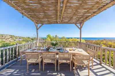 a table and chairs on a deck with a view of the ocean at Villa Rocca Rossa vue exceptionnelle sur la mer in Porto-Vecchio