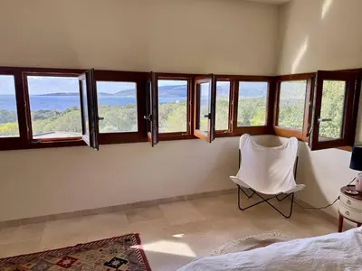 a bedroom with a white chair and windows at Villa d'architecte à Abbartello, vue mer et accès plage in Olmeto