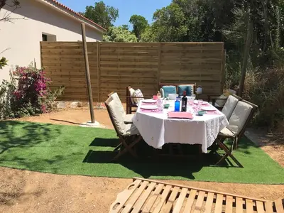 a table and chairs on a lawn with a table and a bench at Isolella à 50 m de la plage in Pietrosella