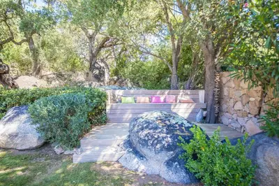 a bench in a garden with trees and rocks at meli melo in Pinarellu