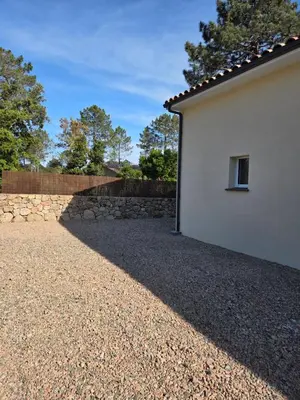 a house with a stone wall next to a building at Agréable T2 proche Porto Vecchio in Sotta