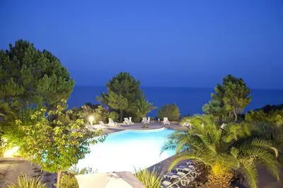 a swimming pool with palm trees and umbrellas at Le Thyreneen in Sari Solenzara