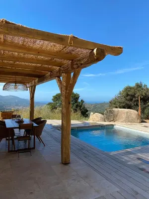 a wooden patio with a table and a swimming pool at Beautiful Stone House With Sea View In Corsica in Sari-dʼOrcino