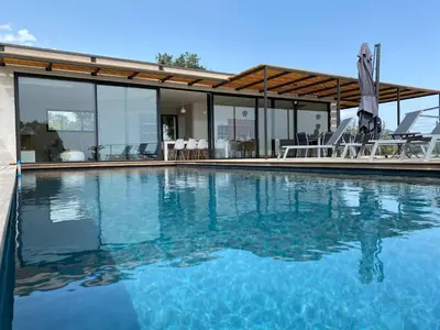 a swimming pool with blue water in front of a house at Rostalana in Pinarellu