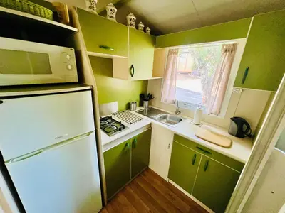 a small kitchen with green cabinets and a white refrigerator at Chalet A tout confort à deux pas des plages in Pianottoli-Caldarello