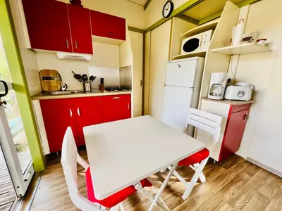a small kitchen with a white table and red cabinets at Chalet N tout confort à deux pas des plages in Pianottoli-Caldarello