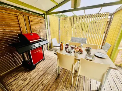 a patio with a table and a grill on a deck at Chalet N tout confort à deux pas des plages in Pianottoli-Caldarello