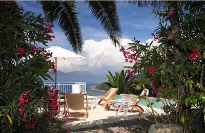 a patio with chairs and an umbrella and the ocean at Villa Gardelina in Campomoro