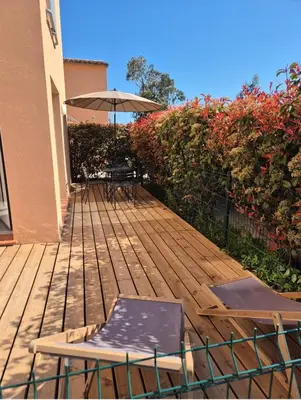 a wooden deck with a table and an umbrella at Les hameaux de Saint Cyprien - appartement avec jardin et piscine in Lecci