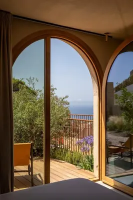 an open patio door with a view of the ocean at Hôtel Mylos - Cargèse, Piscine Intérieure et Extérieure in Cargèse