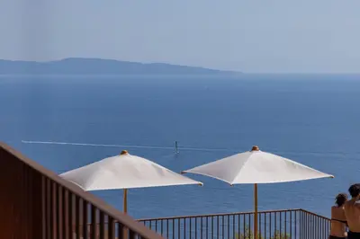 three white umbrellas on a balcony looking at the ocean at Hôtel Mylos - Cargèse, Piscine Intérieure et Extérieure in Cargèse