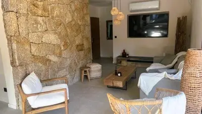 a living room with a stone wall with a tv at Villa Isula Bella, 8 pers, piscine chauffée, proche plage in Sainte-Lucie de Porto-Vecchio