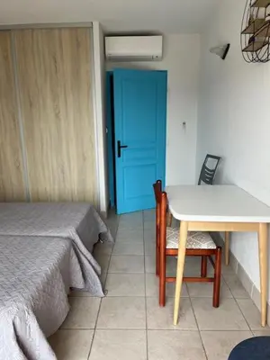 a room with two beds and a table and a blue door at Ajaccio appartement vue mer in Ajaccio