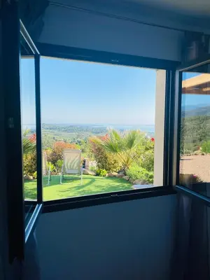 a window with a view of a chair in a yard at Magnifique appartement vue mer et montagne à Solenzara Corse in Sari Solenzara