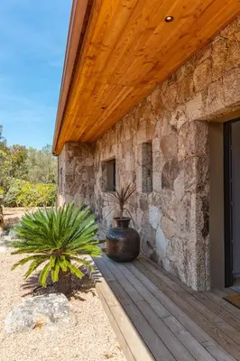 a stone building with a wooden porch with two potted plants at Villa Campemu Di Lecci in Lecci