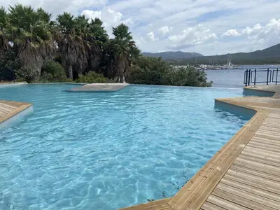 a swimming pool next to a body of water at APPT T3 terrasse dans résidence bord de mer avec piscine in Pianottoli-Caldarello