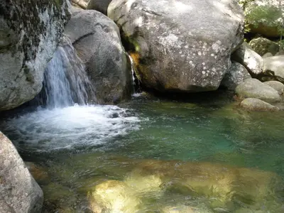 a waterfall in a pool of water next to some rocks at U Paesu in Zonza