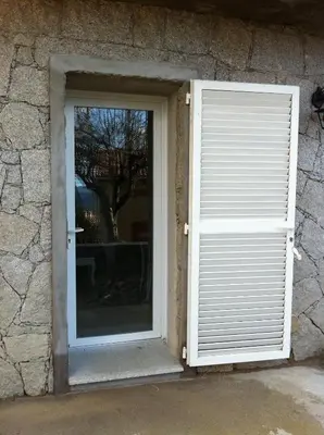 a door with a window in a stone building at U Paesu in Zonza