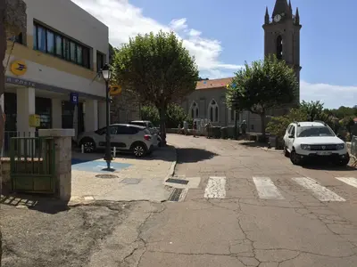 a street with parked cars and a church with a clock tower at U Paesu in Zonza