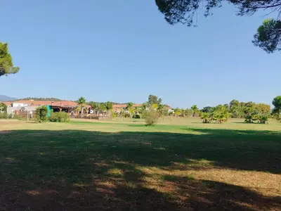 a park with a green field with trees and buildings at Appartement avec jardin piscine et plage 100 m in Poggio-Mezzana