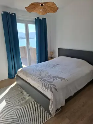 a bedroom with a bed with blue curtains and a window at Appartement vue mer à 1min de la plage in Grosseto-Prugna